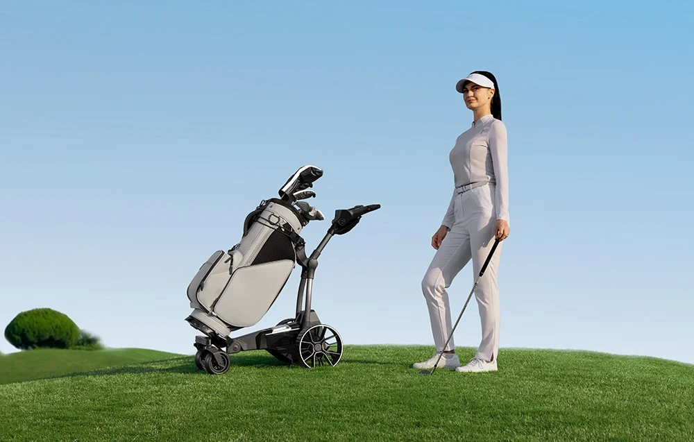 Golfistka stoi z kijem obok automatycznego wózka golfowego NAVEE Birdie 3X z torbą na tle nieba.